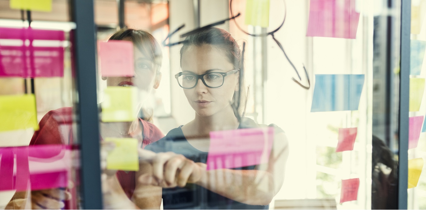 Two business women working together on wall glass